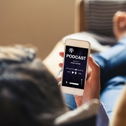 Woman at home holding a mobile phone with podcast app in the screen