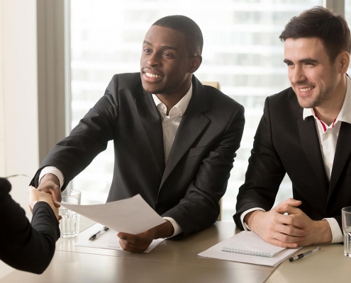 Two cheerful black and white recruiters welcoming female applicant on job interview, african and caucasian hr managers greeting candidate for vacant position, handshaking and good first impression